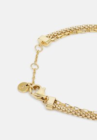 Bracciale in metallo dorato con design a maglie texturizzate, chiusura a gancio, e catena regolabile con un dettaglio a forma di targa rotonda.