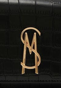 Svart faux krokodilleder veske med et fremtredende gull "SM"-logo. Teksturen er glatt med en blank finish.