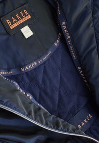 Marineblå quiltet jakke med inderside i glat satin, med orange "BAKER by TED BAKER" label og trimdetaljer.