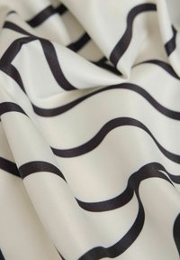 Tissu crème avec de larges rayures ondulées noires, présentant une texture lisse et un léger éclat, élégamment drapé et plié.