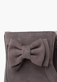 Bottines en suède gris avec une surface texturée, un accent de nœud proéminent à l'arrière, et des coutures contrastées sur les bords.