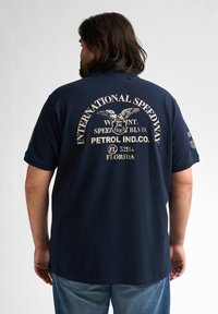 Mörkblå bomulls t-shirt med en stor vit grafisk tryck på baksidan, där det står "INTERNATIONAL SPEEDWAY" och en örn-design.