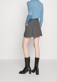 Jupe plissée grise avec poches latérales, associée à un haut bleu à manches longues, complétée par des bottines noires brillantes à talon bloc.