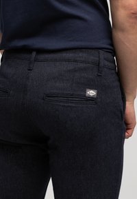 Granatowe teksturowane spodnie o dopasowanym kroju, z dwoma tylnymi kieszeniami i małą, markową metką na prawej kieszeni.