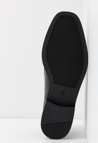 Semelle d'une chaussure habillée noire avec motif de grip texturé, talon lisse et taille 37 marquée près du centre.