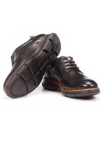 Zapatos de cuero negro con un acabado suave, punta redonda, acentos marrones y suelas de goma texturizadas. Los cordones tienen costuras contrastantes.