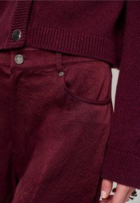 Bordeaux gebreide trui met geribde manchetten, gecombineerd met gestructureerde bordeauxbroek met een subtiel kreukpatroon en metalen knopen als accent.