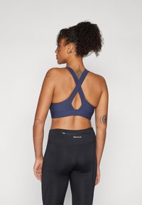 Mornarska športna modrček z dizajnom športnih naramnic, z izreza v obliki ključa in teksturiranega materiala, v kombinaciji z visokim črnim leggingom.