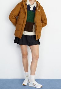 Brown puffer jacket, green and brown knit sweater, black skirt, white sneakers with textured accents and logo. Simple, casual outdoor attire.