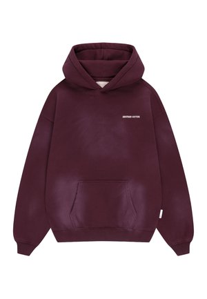 Tumši sarkans kapuci ar priekšpusi kabatu un mazu baltu uzrakstu "ANOTHER COTTON" uz kreisā krūšu puses.