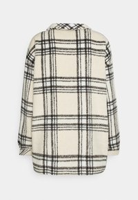 Veste à manches longues couleur crème avec un grand motif à carreaux noir et gris, vue de dos.