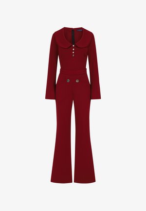 Červený overal s dlouhým rukávem, kulatým límcem, zapínáním na knoflíky vpředu, vysokým pasem, rozšířenými nohavicemi a dekorativními knoflíky na kapsách.