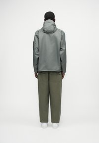 Γκρι φούτερ μπουφάν με λεία υφή, σε συνδυασμό με ανοιχτό πράσινα παντελόνια φαρδιάς γραμμής; και τα δύο ρούχα έχουν χαλαρή εφαρμογή και ελάχιστες λεπτομέρειες.