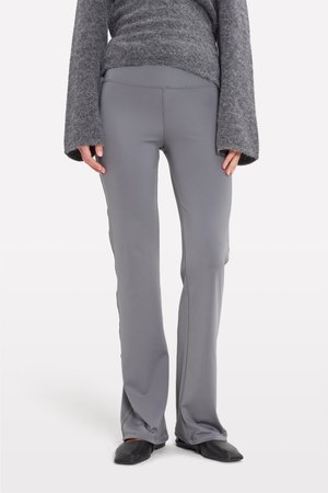 Gray, fitted athletic pants with a smooth texture, flared bottom, and side seam detailing. Worn with a gray sweater and black flats.