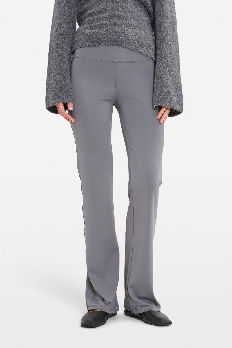 Gray, fitted athletic pants with a smooth texture, flared bottom, and side seam detailing. Worn with a gray sweater and black flats.