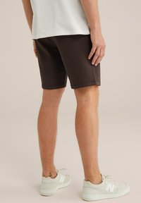 Bruine broeken met een reguliere pasvorm, gecombineerd met witte sneakers. De shorts hebben een zachte textuur en een schoon, eenvoudig ontwerp.