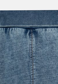 Joggers in denim con vita a coste blu scuro, corpo blu chiaro, tessuto testurizzato e cuciture dorate lungo la cucitura laterale.