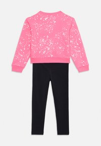 Felpa rosa con macchie bianche, colletto rotondo e polsini a coste abbinata a leggins neri. Entrambi realizzati in un tessuto morbido ed elastico.