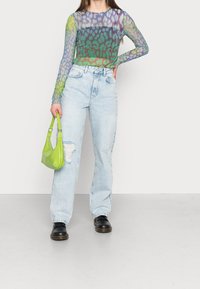 Transparente Langarmbluse mit mehrfarbigem Tiermuster, kombiniert mit hochgeschnittenen hellblauen Jeans und einer kleinen grünen Handtasche.