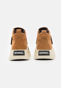 Bruna mockasin hög-top sneakers med svarta accenter, vita gummisulor och svart "SOREL"-logotyp på hälen. Strukturerad detaljering på sulan.