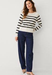 Gestreepte trui in crème en zwart, met een ronde hals en lange mouwen. Gecombineerd met hooggewaadje wijde jeans in het blauw en beige hakken.
