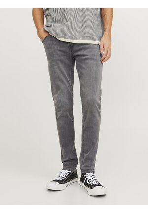 Jeans en denim gris avec une coupe slim, un délavage léger et une distorsion subtile. Associés à des baskets noir et blanc pour un look décontracté.