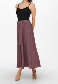 Černý přiléhavý top s tenkými ramínky doplněný středně dlouhou, plisovanou mauve sukní s uvázaným páskem v pase. Look doplňují béžové podpatky.