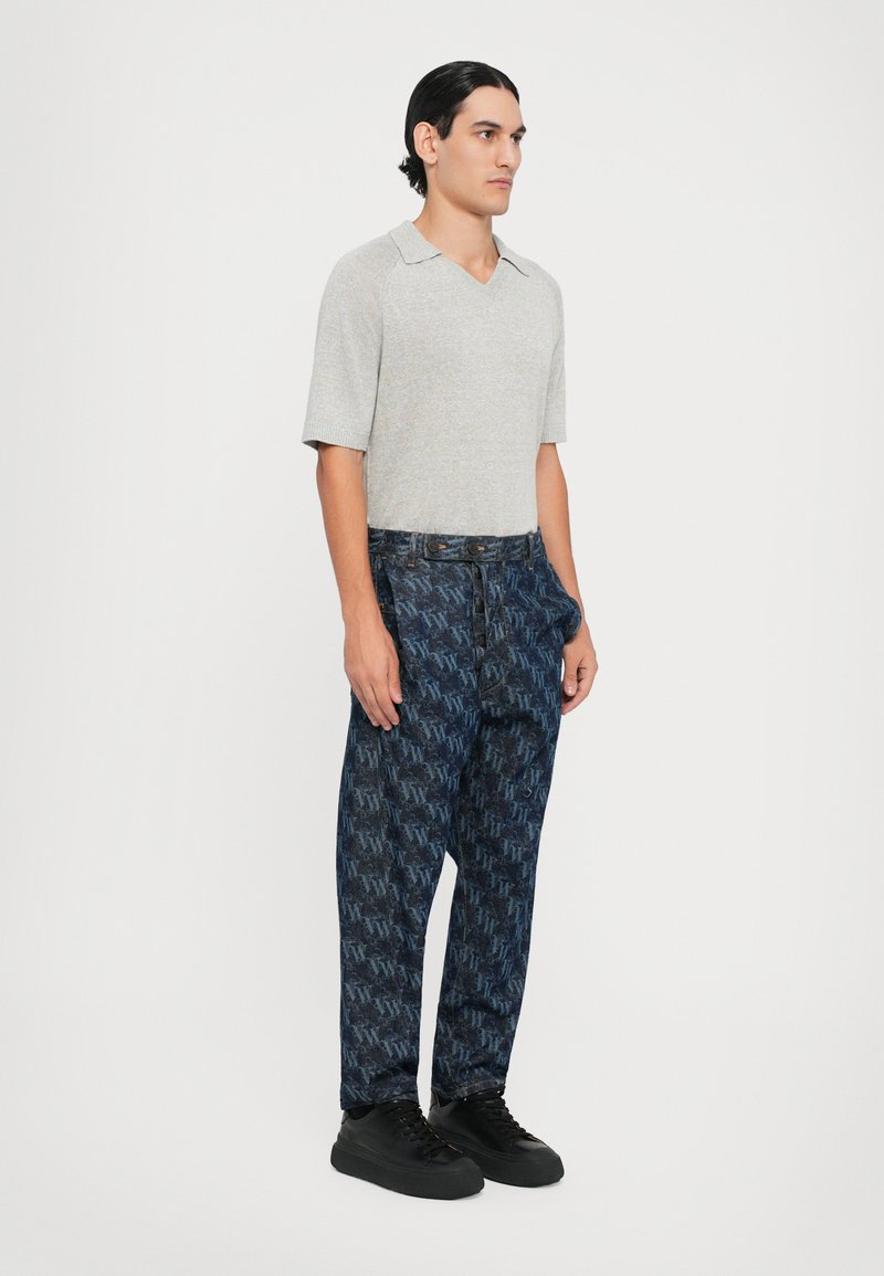 Grijze korte mouwen gebreide polo met V-hals, gecombineerd met blauwe pantalon met patroon in logo-print, aangevuld met zwarte sneakers.