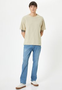 Camiseta de manga corta beige con un corte relajado, combinada con jeans rectos de color azul claro y zapatillas blancas con suelas marrones.