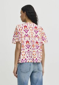 Short-sleeve blouse in lightweight fabric, featuring a colorful floral pattern in pink, orange, and purple on a cream background.