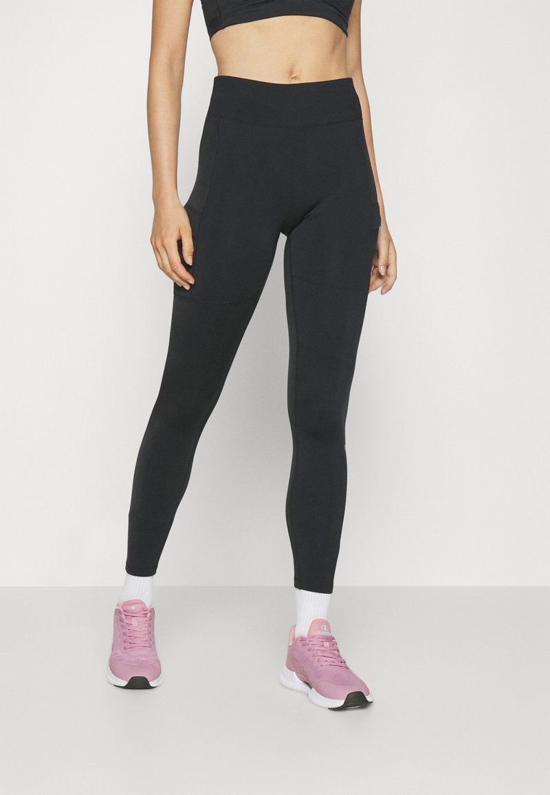 Svarta högmidjade leggings med en elegant design, sidofickor och en slät textur. Matcher med rosa sportskor och vita strumpor.