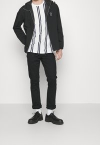 Svart lättviktsjacka med huva, vitrandig t-shirt, svarta jeans och svarta snörskor. Enkel design, minimala detaljer.