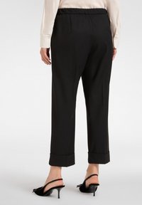 Zwarte tapered broek met een elastische tailleband, opgerolde boorden en een gladde textuur, gecombineerd met zwarte slingback hakken.