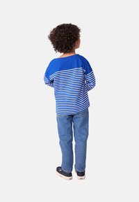 Blaues Langarmhemd mit weißen horizontalen Streifen, Jeans in Denim-Optik und dunklen Schuhen. Rückansicht zeigt einen lockeren Schnitt und runden Ausschnitt.