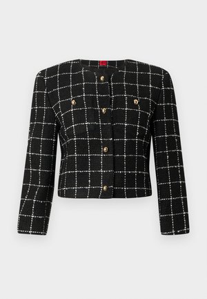 Jachetă scurtă neagră cu un model de grilaj alb, cu nasturi aurii și un decolteu rotund. Fabricată dintr-un material texturat, cu mâneci lungi.