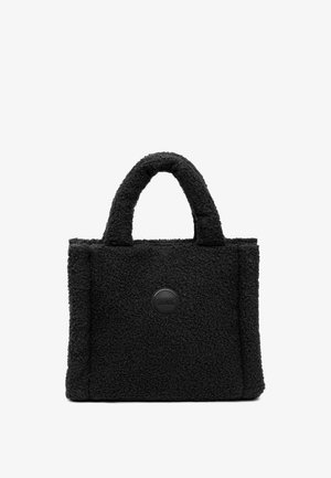 Sac fourre-tout en velours noir avec un extérieur texturé et duveteux, des poignées arrondies et un patch logo noir en forme de cercle. Forme rectangulaire avec des détails cousus.