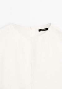 White top with a round neckline and a back zipper. Made from smooth fabric. Label visible at the back, reading "Massimo Dutti, made in Portugal."