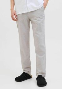 Pantalons droit gris clair en tissu lisse avec une texture subtile. Portés avec des sabots noirs avec un détail de boucle.