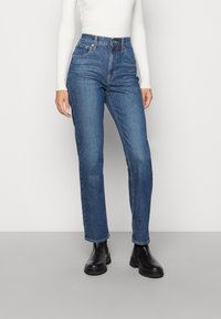 Tmavě modré, vysoko waisted džíny se rovným střihem, s předními kapsami a kontrastním šitím, spárované s černými kotníkovými botami.