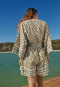 Tiskovaný kimono styl oděv s krátkými rukávy, s žluto-černým vzorem listů, kontrastními okraji a volným střihem.
