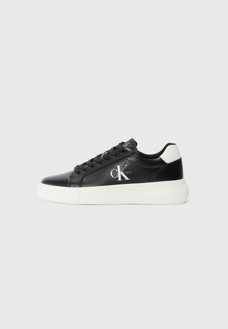 Baskets basses en cuir noir avec semelle blanche et languette au talon, avec le logo "cK" de Calvin Klein sur le côté et des lacets noirs.