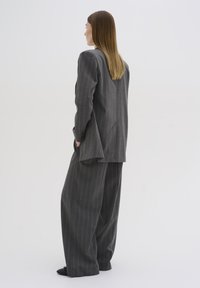 Abito grigio a righe con una vestibilità morbida, caratterizzato da un lungo blazer e pantaloni a gamba larga. Tessuto liscio con spalle sagomate e dettagli discreti per le tasche.