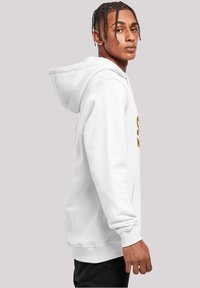 Sudadera blanca con capucha, de mangas largas y bolsillo tipo canguro, con un logo naranja impreso en la parte delantera. Tela suave, corte relajado.