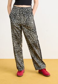 Pantalons imprimés léopard avec une taille élastique, poches latérales et accents noirs, associés à des baskets rouges. Texture de tissu lisse.