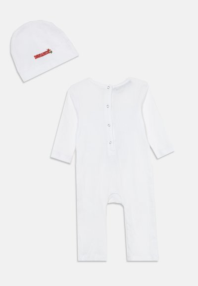 Body bébé blanc à manches longues avec pressions au dos, présenté avec un bonnet blanc assorti comportant un petit dinosaure rouge et jaune brodé.