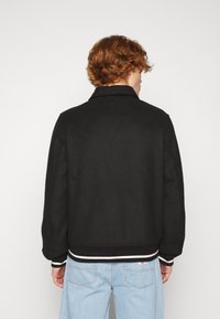 Black bomber jacket made of a soft fabric. Features white striped accents on the cuffs and hem. Classic collar and relaxed fit.