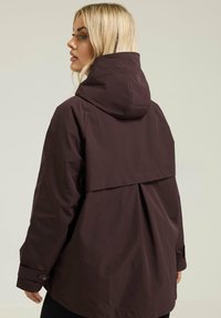 Veste imperméable bordeaux avec capuche, un détail de rabat à l'arrière et des poignets boutonnés. Fabriquée en tissu léger avec une finition mate.