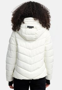 White puffer jacket with a hood, featuring chevron quilting and a black logo tag on the back. Material appears soft and textured.