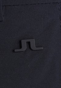 Svart tyg med en mjuk textur har en liten svart logotag formad som ett inverterat bokstav "J" nära sömmen.