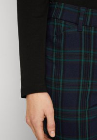 Svart långärmad skjorta i kombination med marinblå rutiga byxor med gröna och svarta ränder, synlig midjeband och fickdetalj.